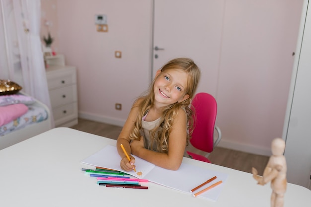 Gelukkig lachend meisje tekent thuis zittend aan tafel met viltstiften