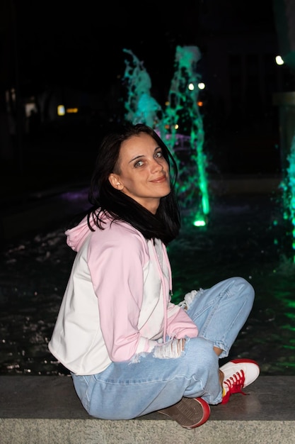 Gelukkig lachend meisje zit 's nachts bij de fontein