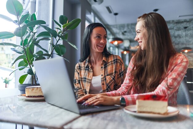 Gelukkig lachend moeder en vrolijke jonge dochter kijken naar video-inhoud op een laptop en hebben een goede tijd samen in een café