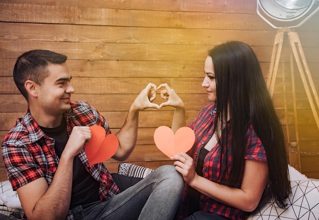 Gelukkig lachend paar verliefd tonen hart met hun vingers en houden twee rode papieren harten Vrouw en man vormen hartvorm op houten achtergrond Liefde concept