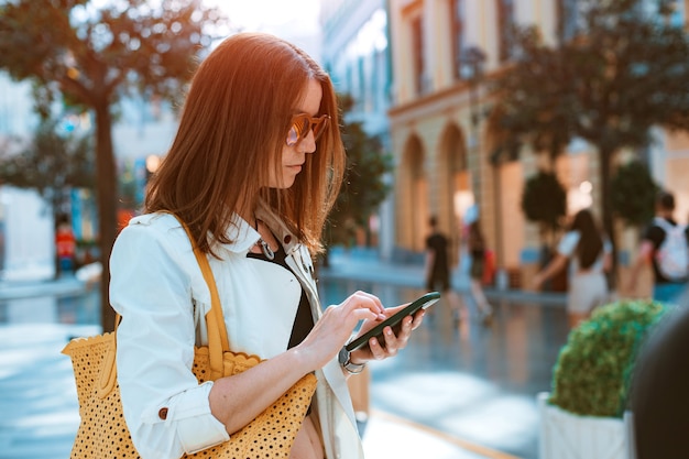 Gelukkig lachend student meisje in modieuze zonnebril loopt buiten in zomerdag met smartphone