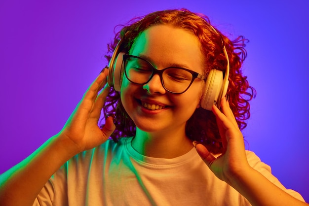 Gelukkig lachend tienermeisje met krullend haar luisteren naar muziek in koptelefoon tegen paarse achtergrond