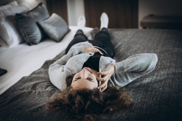 Gelukkig lachend tienermeisje praten via de telefoon liggend op haar rug op het bed