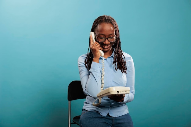 Gelukkig lachend vaste telefoon operator met een gesprek op bedrade telefoon op blauwe achtergrond. Zelfverzekerde positieve jonge volwassen vrouw die een klant beantwoordt die om advies vraagt.