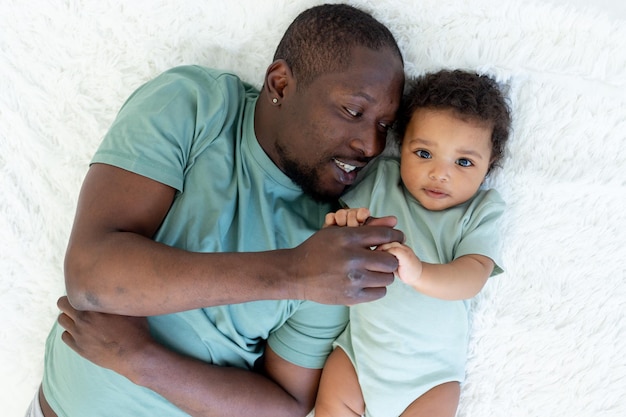 Gelukkig lachende Afro-Amerikaanse vader met zoontje op bed thuis knuffelen, gelukkige familie, vaderdag