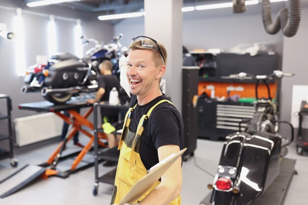 Gelukkig lachende automonteur of slotenmaker met klembord in werkplaats auto service en onderhoud