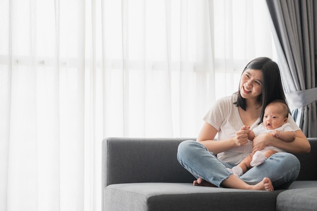 Foto gelukkig lachende aziatische moeder die plezier heeft met haar dochterbaby op de bank thuis