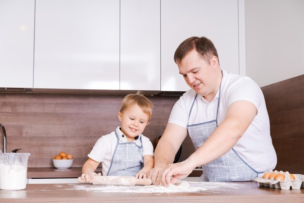 Gelukkig lachende blanke familie in schorten koken en deeg kneden op een houten