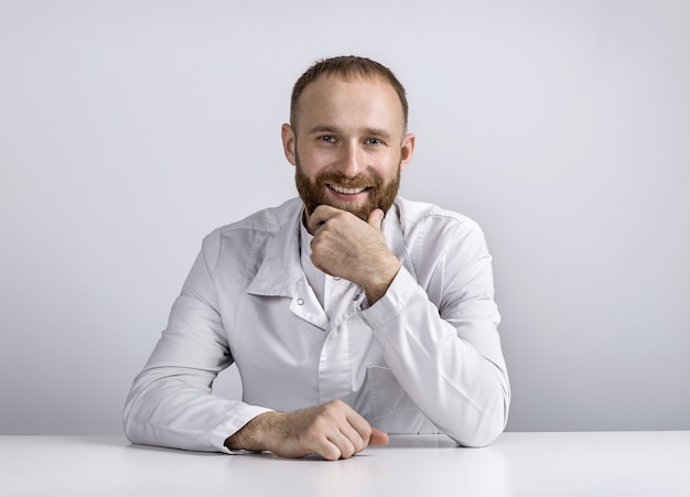 Gelukkig, lachende dokter in wit gewaad zit aan tafel. portret.