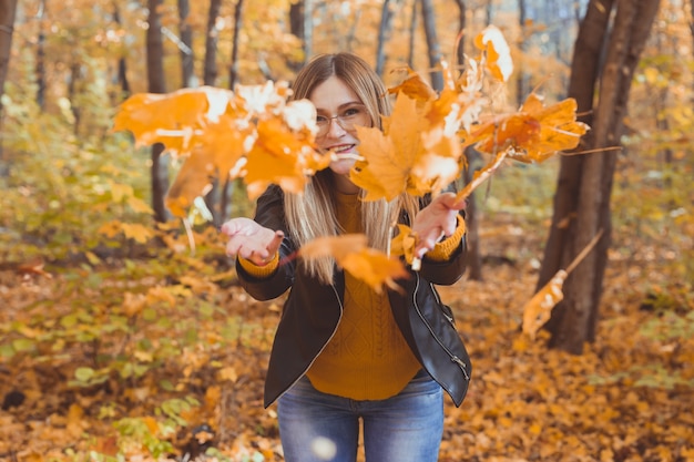 Gelukkig lachende jonge vrouw die bladeren gooit in het herfstseizoen van het park