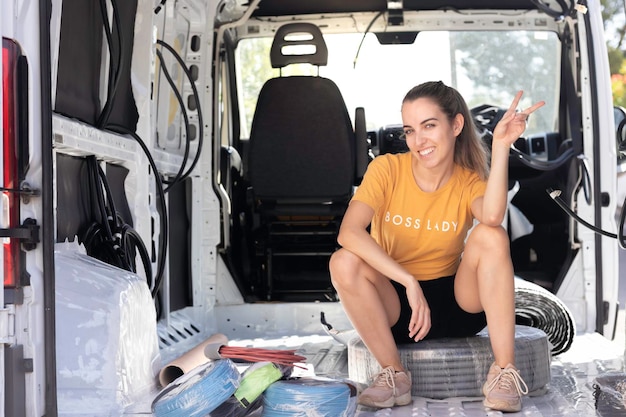 Gelukkig lachende jonge vrouw met gelukkig V-teken op zoek naar camera zittend in een camper in conversieproces