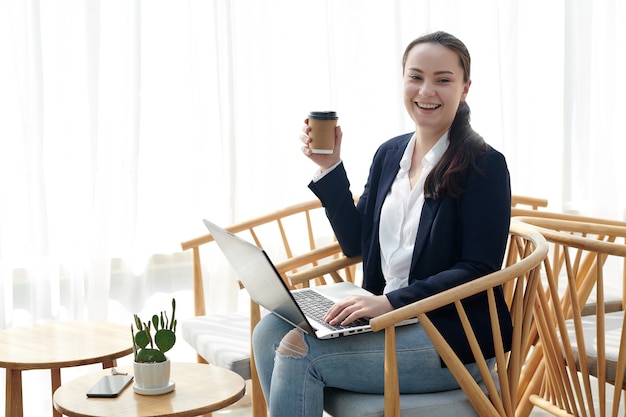 Gelukkig lachende jonge vrouwelijke ondernemer met laptop koffie drinken in café