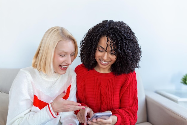 Gelukkig lachende jonge vrouwen vrienden kijken naar foto's op mobiele telefoon Meisjes hebben plezier Twee vrouwelijke vrienden ontspannen thuis samen praten