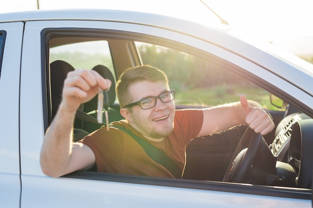 Gelukkig lachende jongeman zit in nieuwe auto met sleutels.