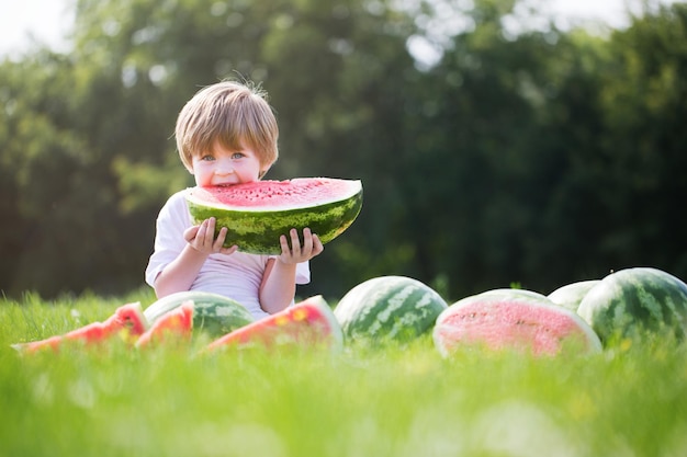 Foto gelukkig lachende jongen die watermeloen buiten eet in het lentepark