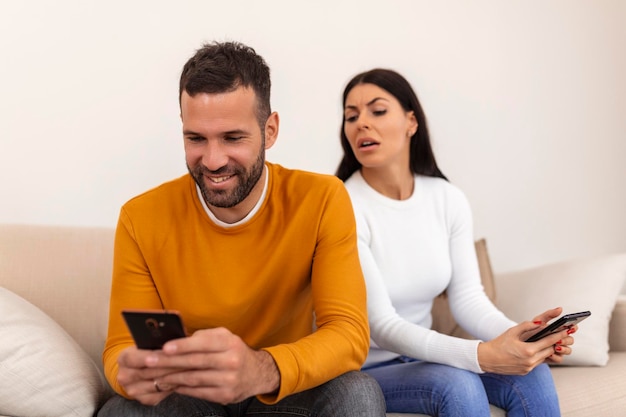 Gelukkig lachende man keerde zijn rug naar de vrouw die het bericht op de telefoon las van zijn geliefde, bezorgde vrouw die naast hem zat en probeerde naar het scherm te gluren Bedrog en ontrouw concept