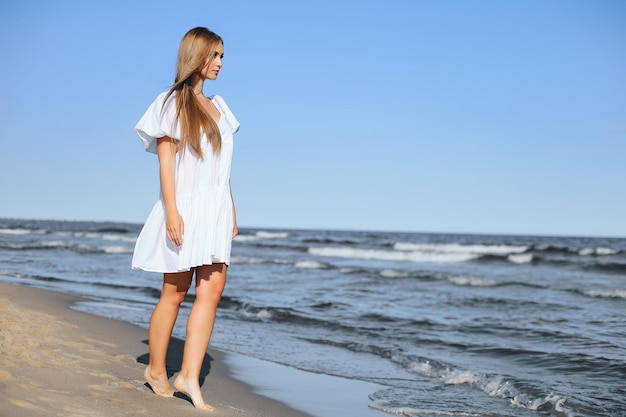 Gelukkig lachende mooie vrouw loopt op het strand van de oceaan in een witte zomerjurk