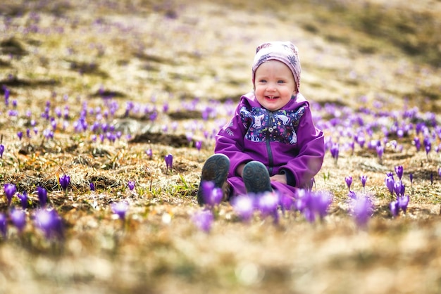 Gelukkig lachende peuter zittend op weide vol violette bloemen