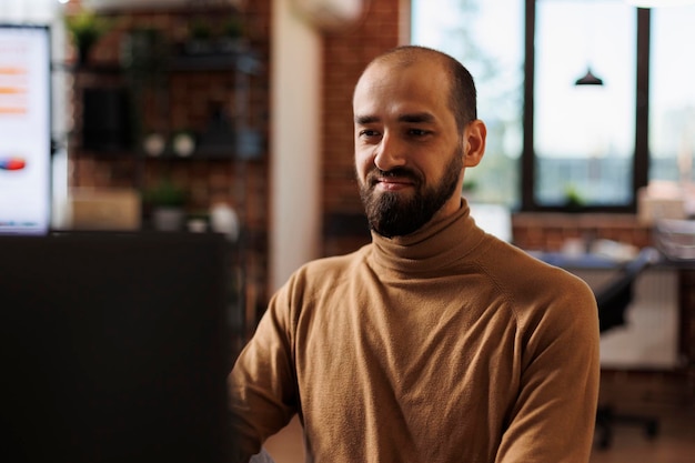 Gelukkig lachende professionele kantoormedewerker die naar financiële grafieken kijkt terwijl hij aan het bureau zit met een werkcomputer. Jonge volwassen ondernemer die financiële ideeën en managementgrafieken ontwikkelt.