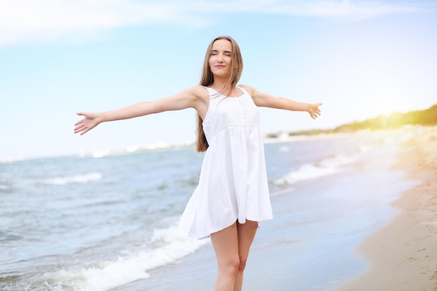 Foto gelukkig lachende vrouw in vrij geluk gelukzaligheid op oceaan strand staande met open handen portret van een multicultureel vrouwelijk model in witte zomerjurk genieten van de natuur tijdens reizen vakantie vakantie