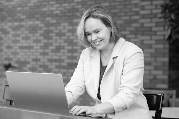 Gelukkig lachende vrouw met behulp van applicatie op digitale laptop in een straatcafé