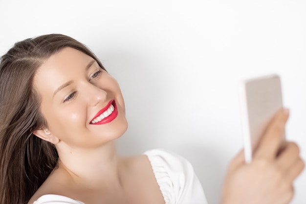 Gelukkig lachende vrouw met smartphone met video-oproep of het nemen van selfie portret op witte achtergrond mensen technologie en communicatie concept