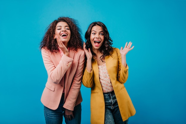 Gelukkig latijns meisje in gele jas poseren binnen Twee dames hebben plezier