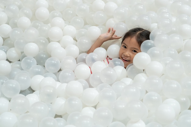 Gelukkig leuk aziatisch kindmeisje die pret met witte plastic ballen in de speelplaats hebben te spelen