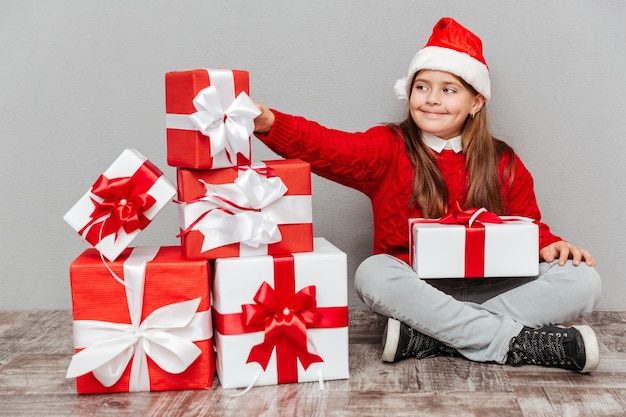 Foto gelukkig lief klein meisje in de hoed van de kerstman die de huidige doos neemt