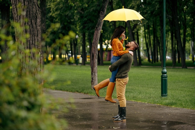 Gelukkig liefde paar omarmen in regenachtige zomerdag. Man en vrouw knuffels onder paraplu in regen, romantische date op wandelpad, nat weer in steegje