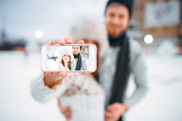 Gelukkig liefdepaar maakt selfie op de ijsbaan. Winter schaatsen in de open lucht, actieve vrijetijdsbesteding, man en vrouw schaatsen samen