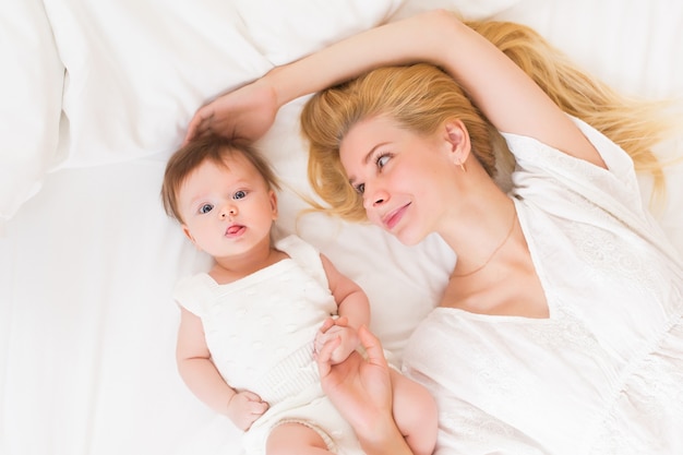 Gelukkig liefdevol familieconcept. mooie moeder speelt met haar babymeisje in de slaapkamer. ze glimlachen en knuffelen samen op wit beddengoed, bovenaanzicht