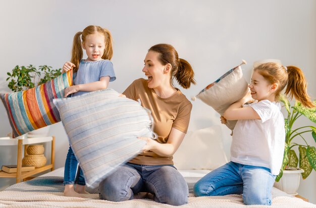 Gelukkig liefdevol gezin! De moeder en de meisjes van haar kinderen vechten thuis tegen kussens op bed.