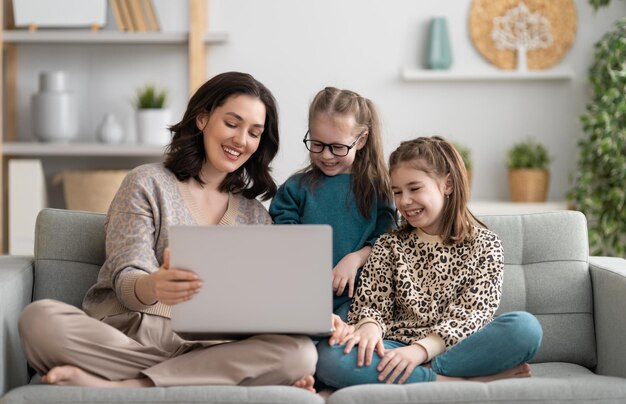 Gelukkig liefdevol gezin. jonge moeder en dochtersmeisjes die laptop met behulp van. grappige moeder en lieve kinderen vinden het leuk om thuis te blijven.