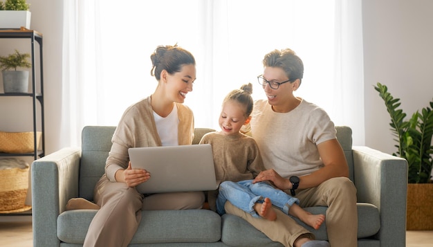 Gelukkig liefdevol gezin. Jonge moeder, vader en dochter die laptop met behulp van. Grappige moeder, vader en lief kind hebben plezier om thuis te blijven.