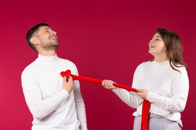 Gelukkig liefdevol paar op een rode achtergrond. Het meisje scheurt een hart uit de borst van de man. Valentijnsdag concept.