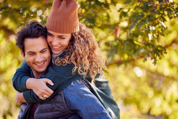 Gelukkig liefdevol stel dat lacht terwijl man vrouw op de rug geeft in herfstpark