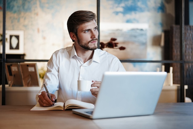 Gelukkig man aan het werk op kantoor, notities maken, zittend aan een bureau