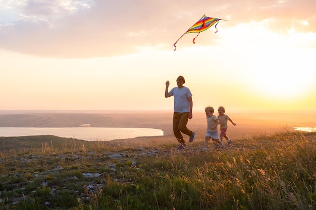 Gelukkig man en twee jongen jongens vader en zonen rennen met vlieger in de natuur bij zonsondergang