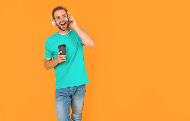 Gelukkig man in blauw shirt draagt koptelefoon met koffie op gele achtergrond ochtend