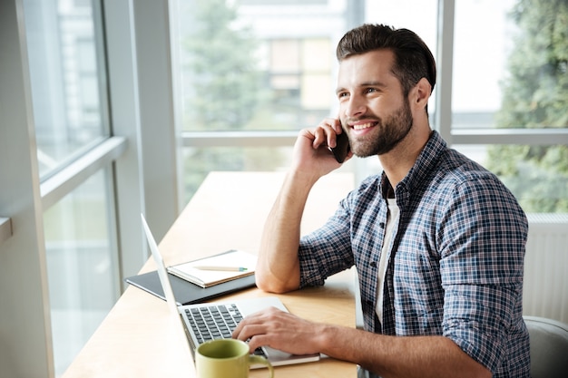 Gelukkig man in kantoor coworking praten via de telefoon.