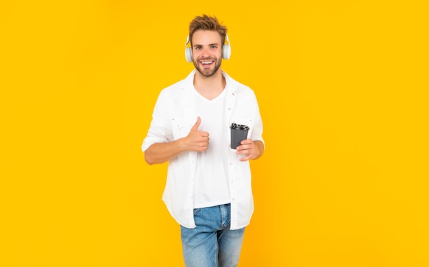 Gelukkig man in witte t-shirt dragen koptelefoon houdt koffiekopje op gele achtergrond levensstijl