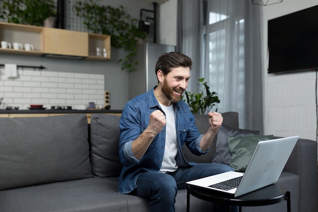 Gelukkig man klaar met het werk aan het project gelukkig werken op de computer met hand omhoog overwinning gebaar man thuis werken met laptop