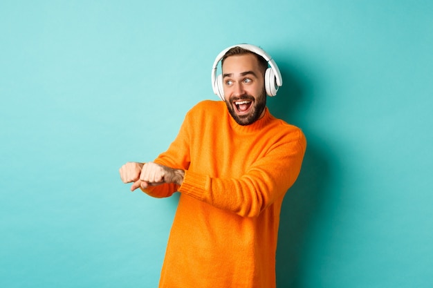 Gelukkig man luisteren muziek in koptelefoon en dansen grappig, staande op turkooizen achtergrond. Kopieer ruimte