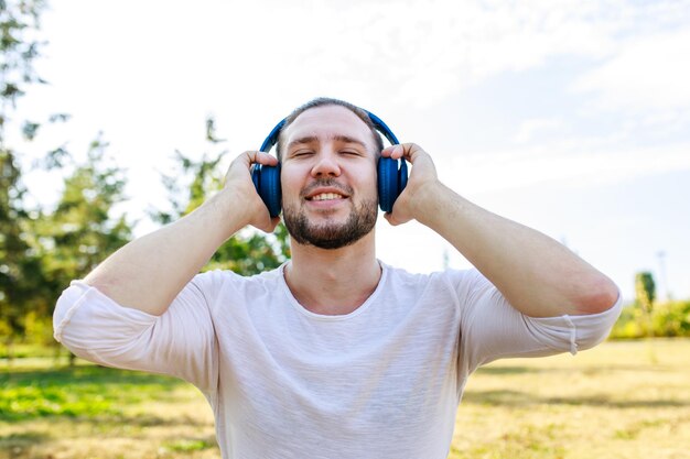Gelukkig man luisteren muziek met koptelefoon in witte blazer buiten in zomer park