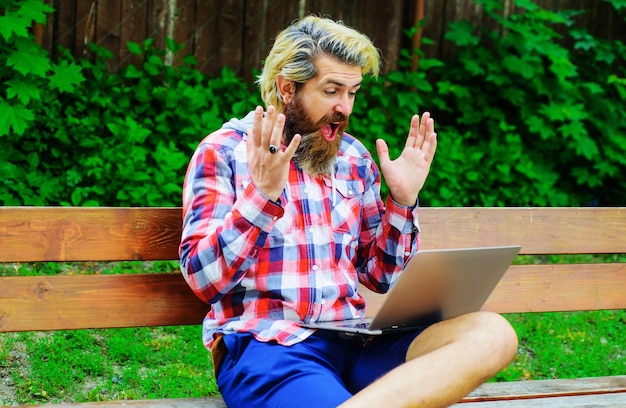 Gelukkig man met laptop in het park freelance geldspel bebaarde man met computer zittend op de bank