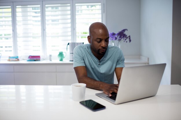 Gelukkig man met laptop met mobiele telefoon en koffiekopje op tafel