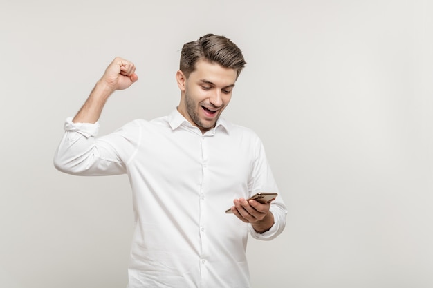 Gelukkig man met mobiele telefoon kijken op het scherm schudden vuisten vieren succes op wit