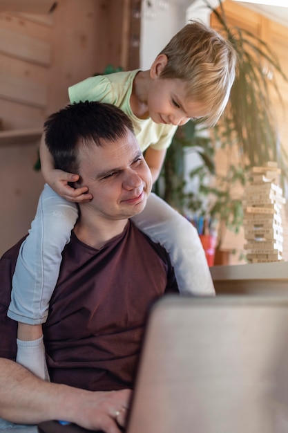 Gelukkig man met vrolijke kinderen met behulp van laptop en oortelefoon tijdens zijn thuiswerk zittend op de bank thuis, kantoor aan huis met samen met kinderen, leven tijdens quarantaine