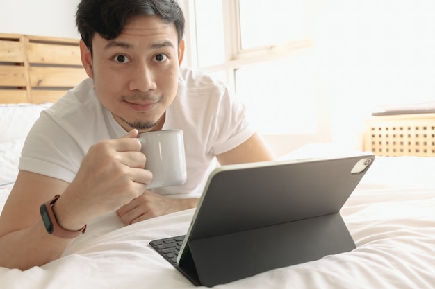 Gelukkig man werkt op zijn tablet met een kopje koffie op het bed